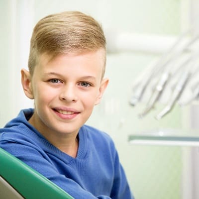 A young boy smiling with dental tools in the background
