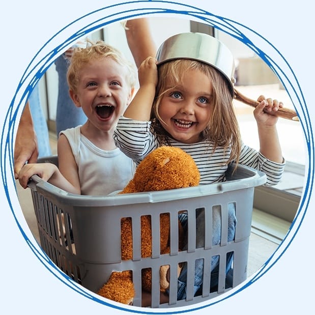 Two young children laughing in laundry basket