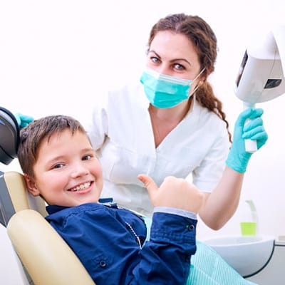 A young boy giving a thumbs up as his dentist looks on behind a mask