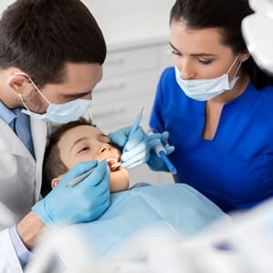 A dentist and dental hygienist examining a young boy’s teeth and gums