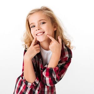 A young girl smiling and pointing to her mouth