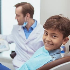 A young boy sitting in the dentist chair smiling