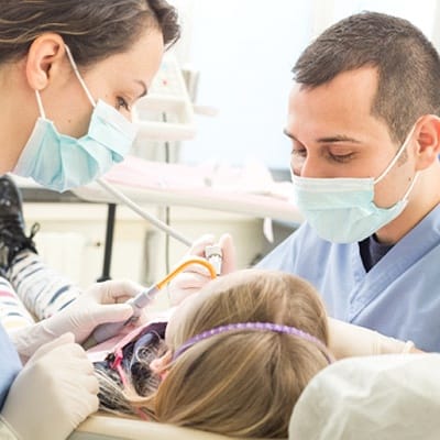 Two dentists performing dental work on a young girl’s mouth