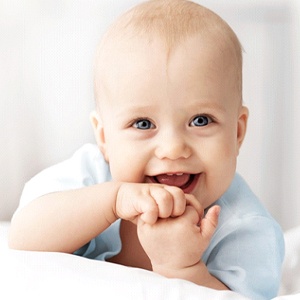 A happy baby with blue eyes lying on its stomach and clasping its hands while smiling