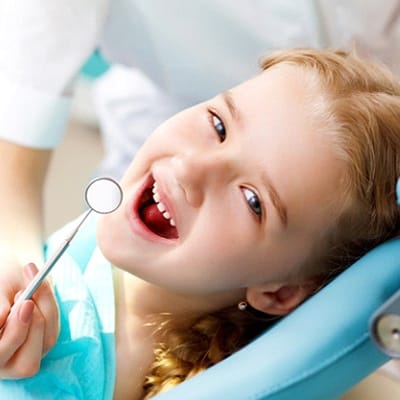 A young, red-haired girl having her teeth checked at the dentist office