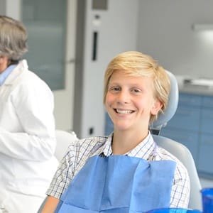 A dentist and dental assistant reviewing paperwork while a young male patient smiles in the dentist’s chair