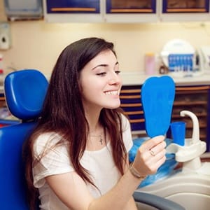 A female teenager looking at her smile in the mirror while seated in the dentist’s chair