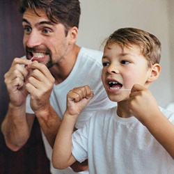 Father and son flossing while looking in the mirror