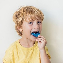 Young boy putting in a blue mouthguard to prevent dental emergencies