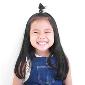 A little girl wearing denim overalls smiling to show off her healthy teeth