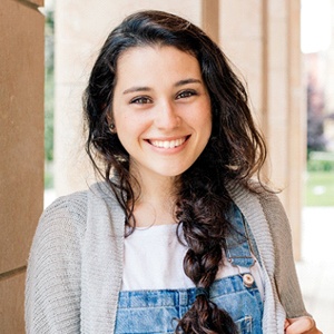 A teenage girl wearing overalls and a cardigan and smiling after undergoing lip and tongue tie treatment