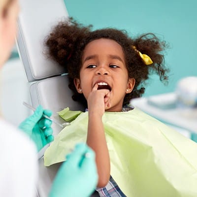 Little girl in dental chair pointing to tooth