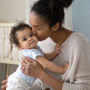 A mother and her child sitting in the nursery while she kisses her baby on the cheek