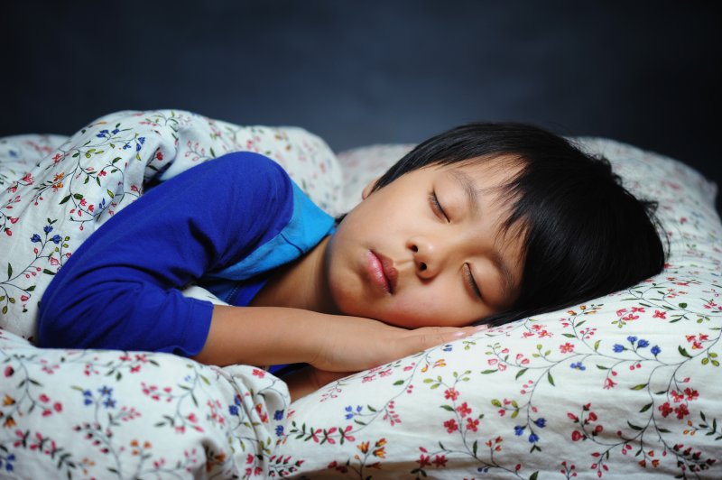 A young boy asleep in bed while lying on his side 