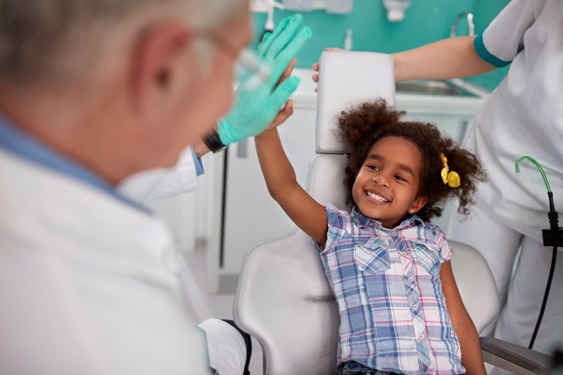a little girl smiling and giving her dentist a high-five after her appointment