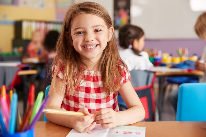 a little girl smiling while seated at her desk at school