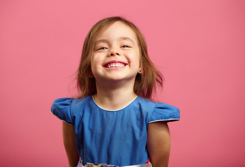 a little girl wearing a blue dress and smiling wide