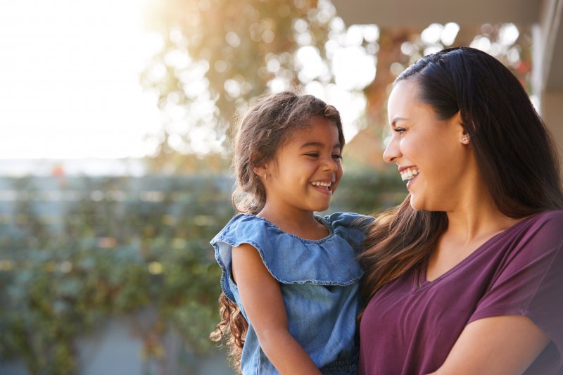 a mother holding her daughter while outside, both smiling and enjoying time together 