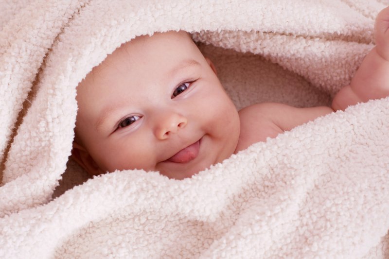 a baby laying covered in a towel and sticking its tongue out after undergoing a frenectomy in McKinney