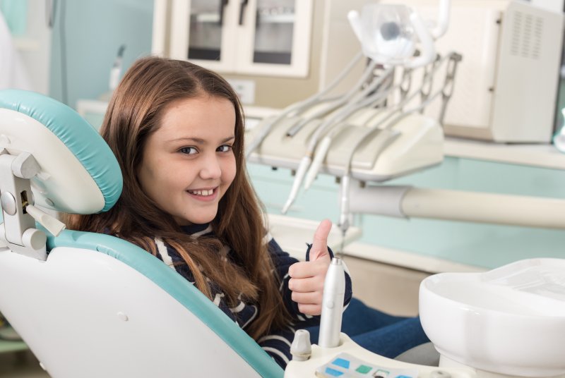 a young girl gives a thumbs up while sitting in the dentist’s chair waiting to undergo laser dentistry in McKinney