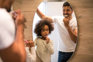 girl brushing teeth with her father