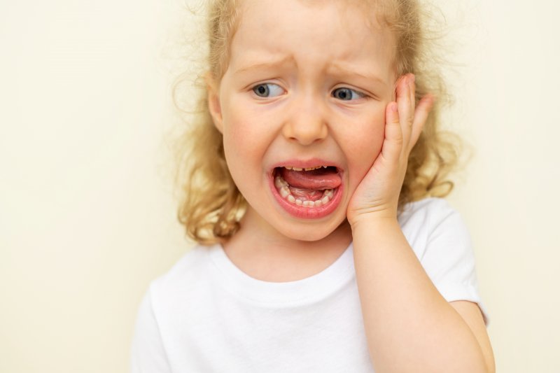 child holding their cheek in pain