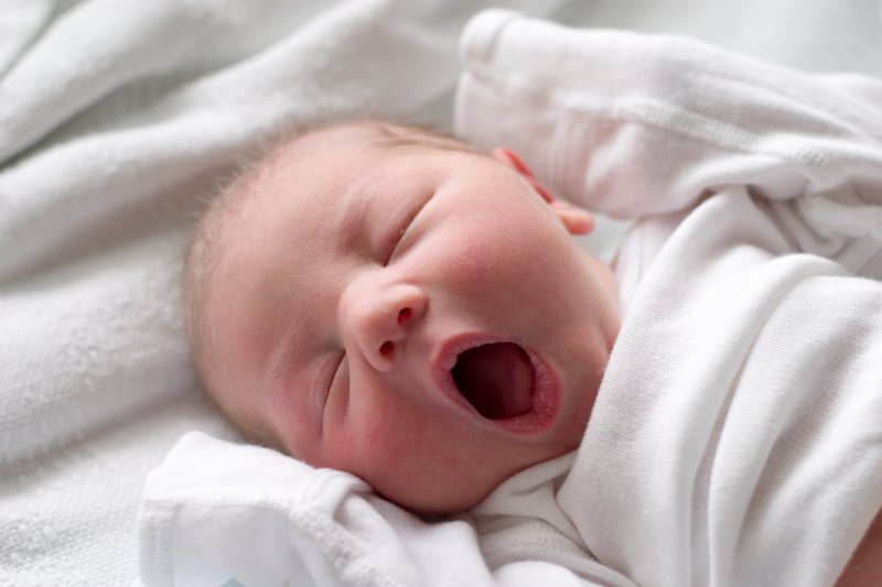 a baby yawning while lying on a bed